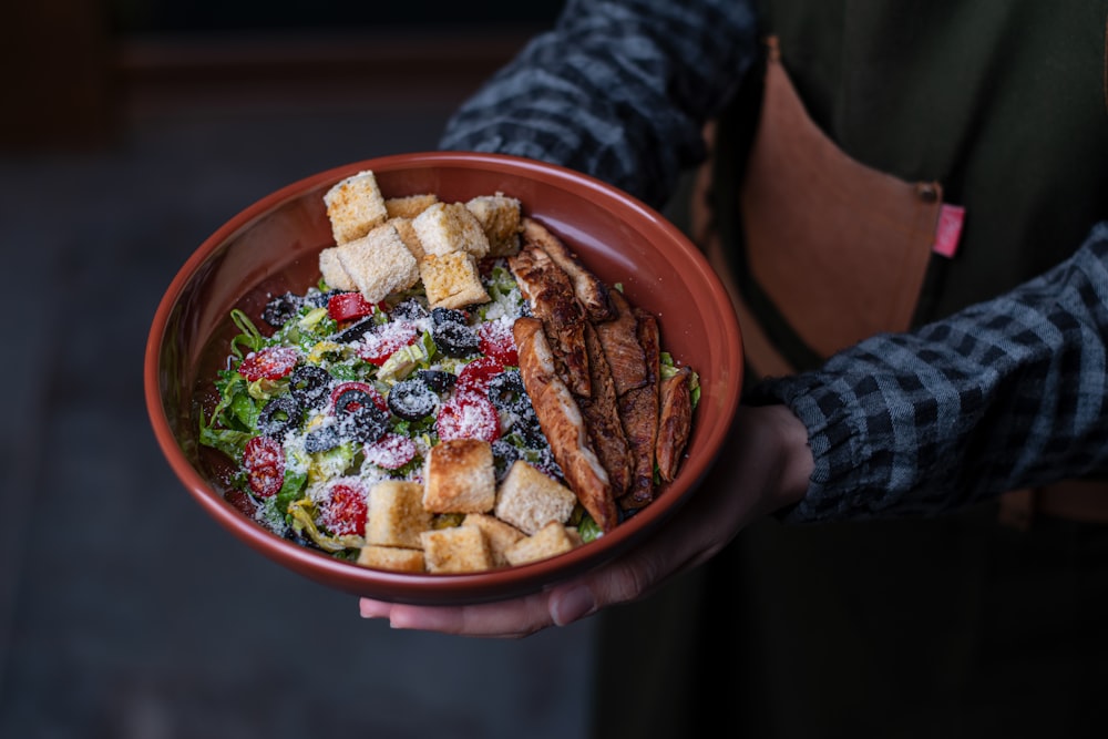 person holding brown ceramic bowl with food