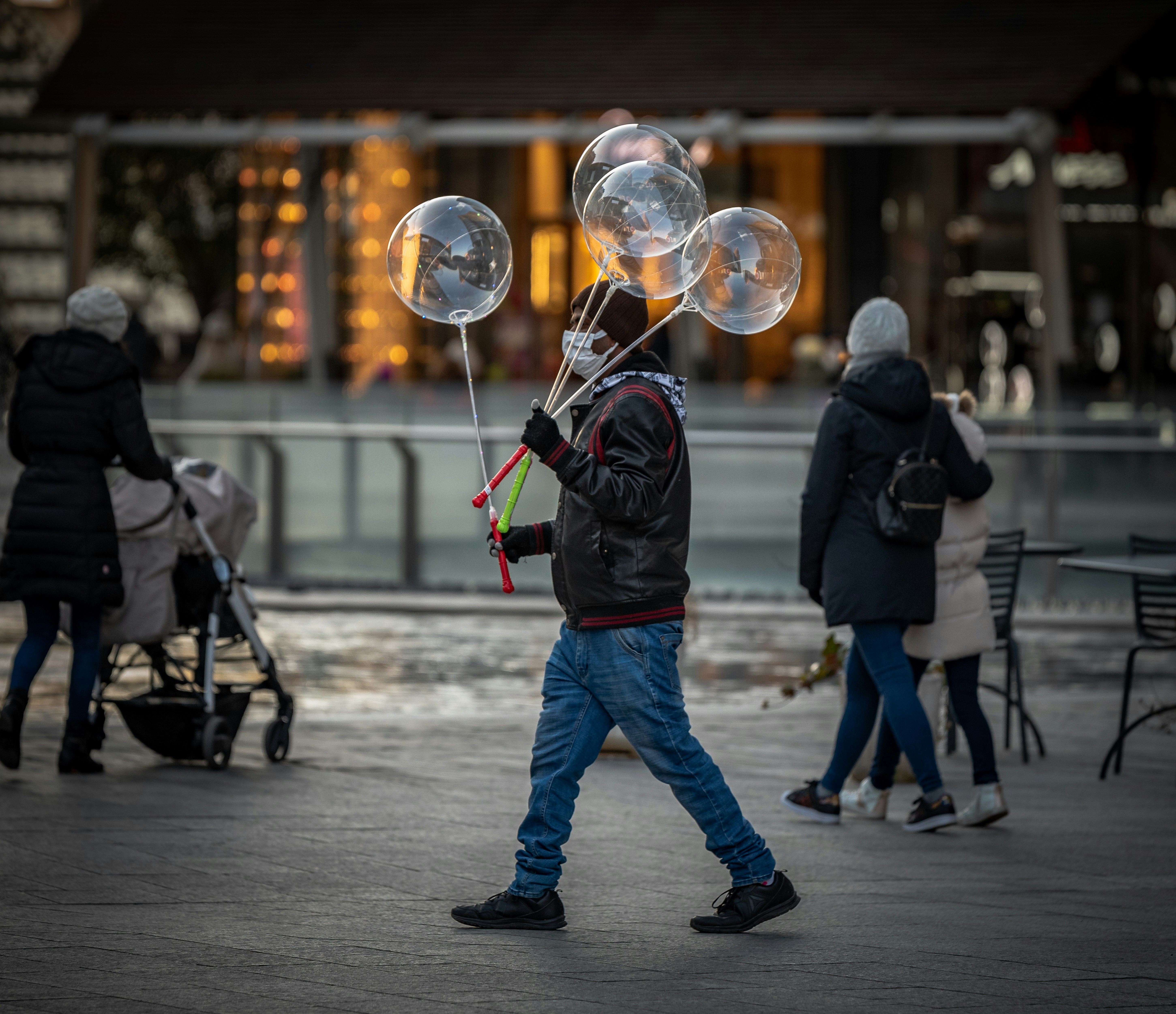 man in black jacket and blue denim jeans holding a bubble stick