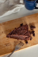 Slice of dark chocolate cake with sea salt flakes beside a glass of cold brew on a charcoal grey surface.