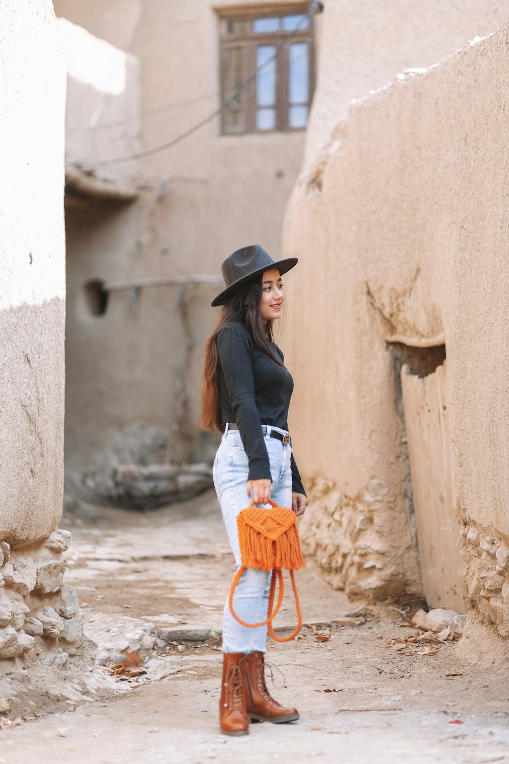 woman in black long sleeve shirt and blue denim jeans wearing black hat standing beside concrete