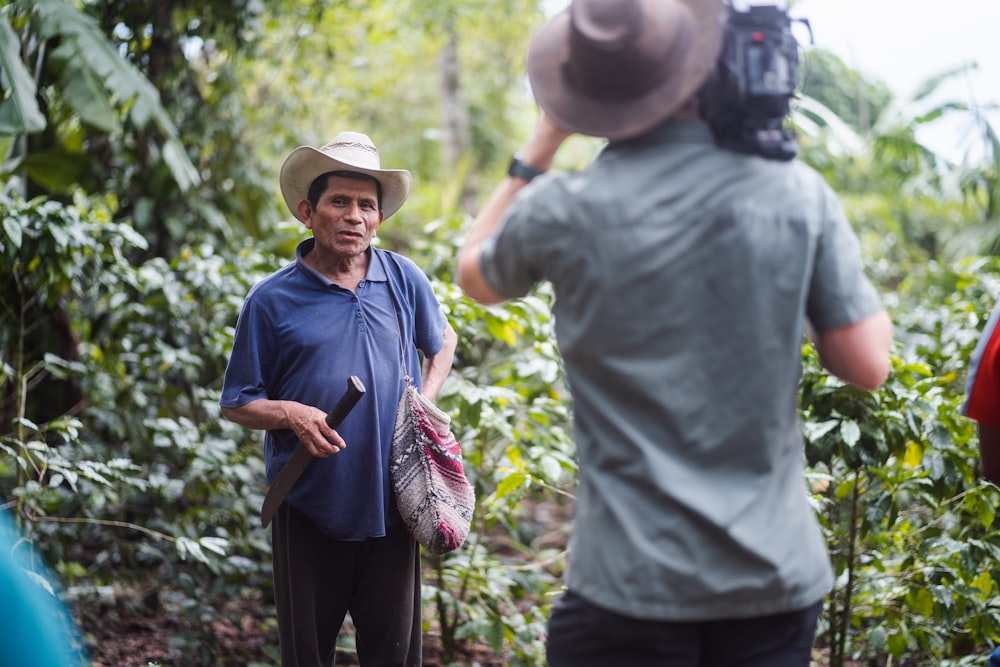 man in blue polo shirt and brown fedora hat standing near green plants during daytime