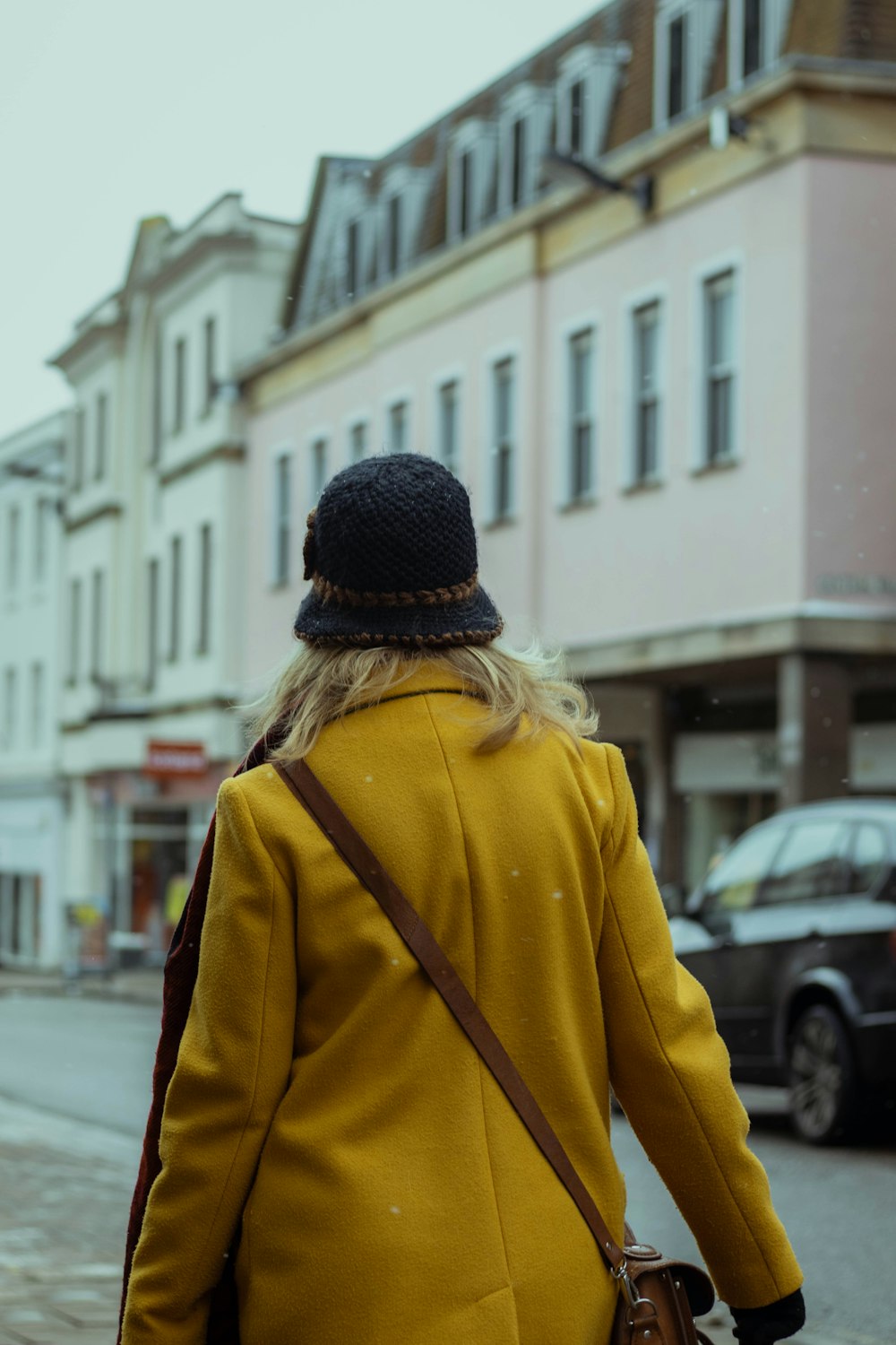 Mujer con chaqueta amarilla y gorra de punto negra caminando por la calle durante el día