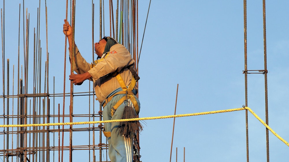 man in yellow shirt and brown pants hanging on brown rope during daytime