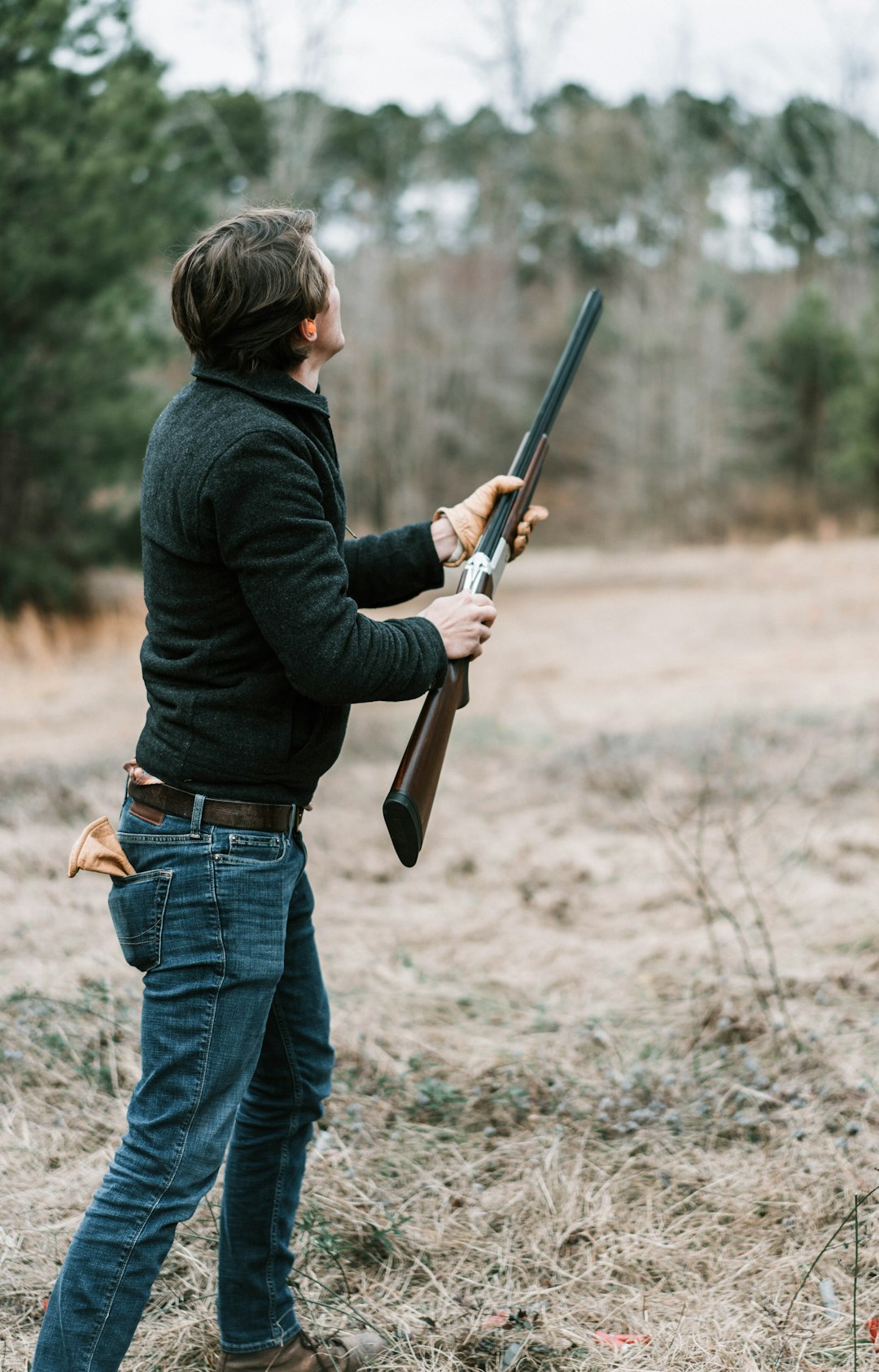 man in black jacket and blue denim jeans holding brown rifle