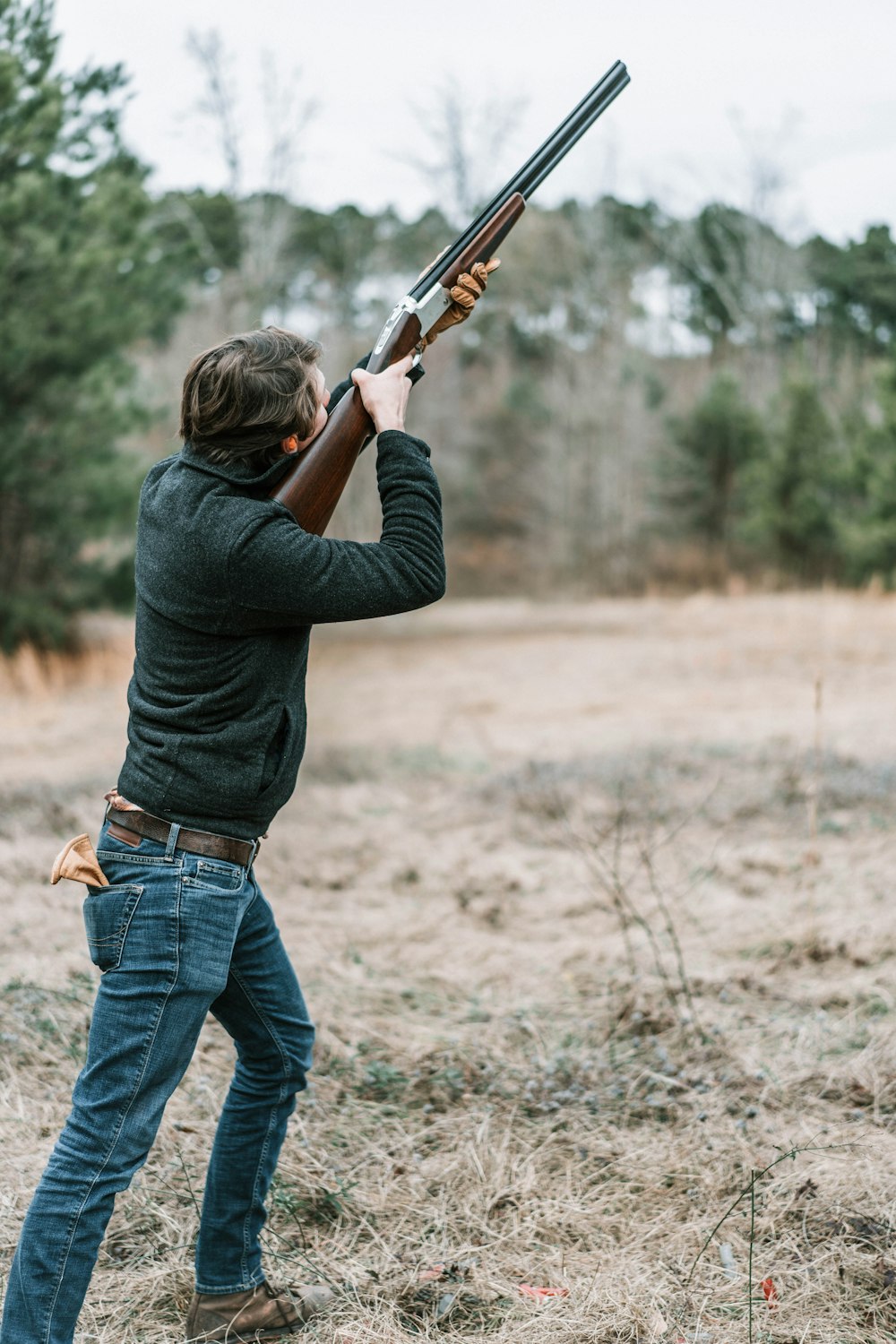 Hombre con camisa negra de manga larga y jeans de mezclilla azul sosteniendo un rifle marrón