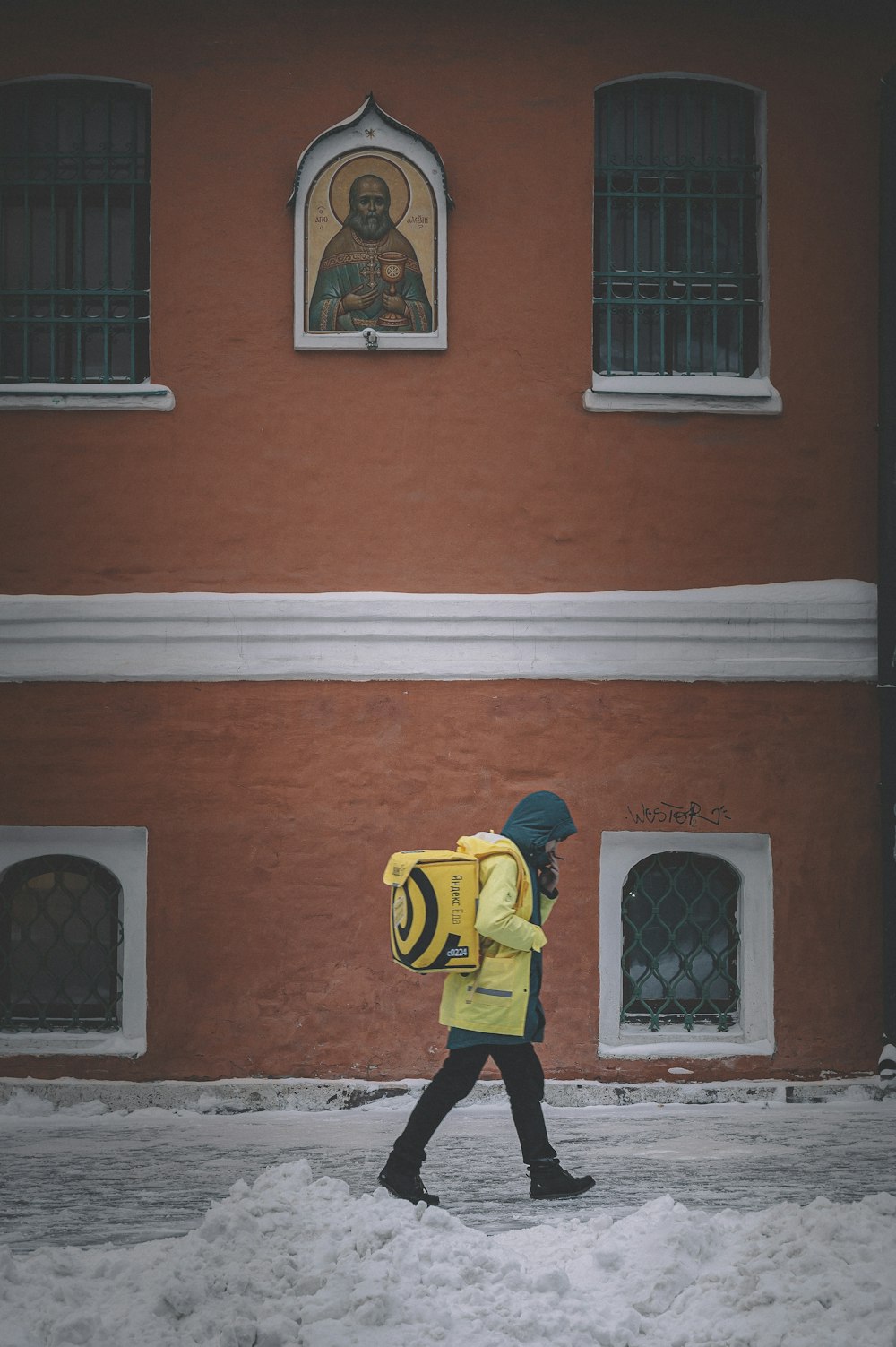 茶色のコンクリートの建物の前に立つ黄色と黒のジャケットと黒いズボンの男