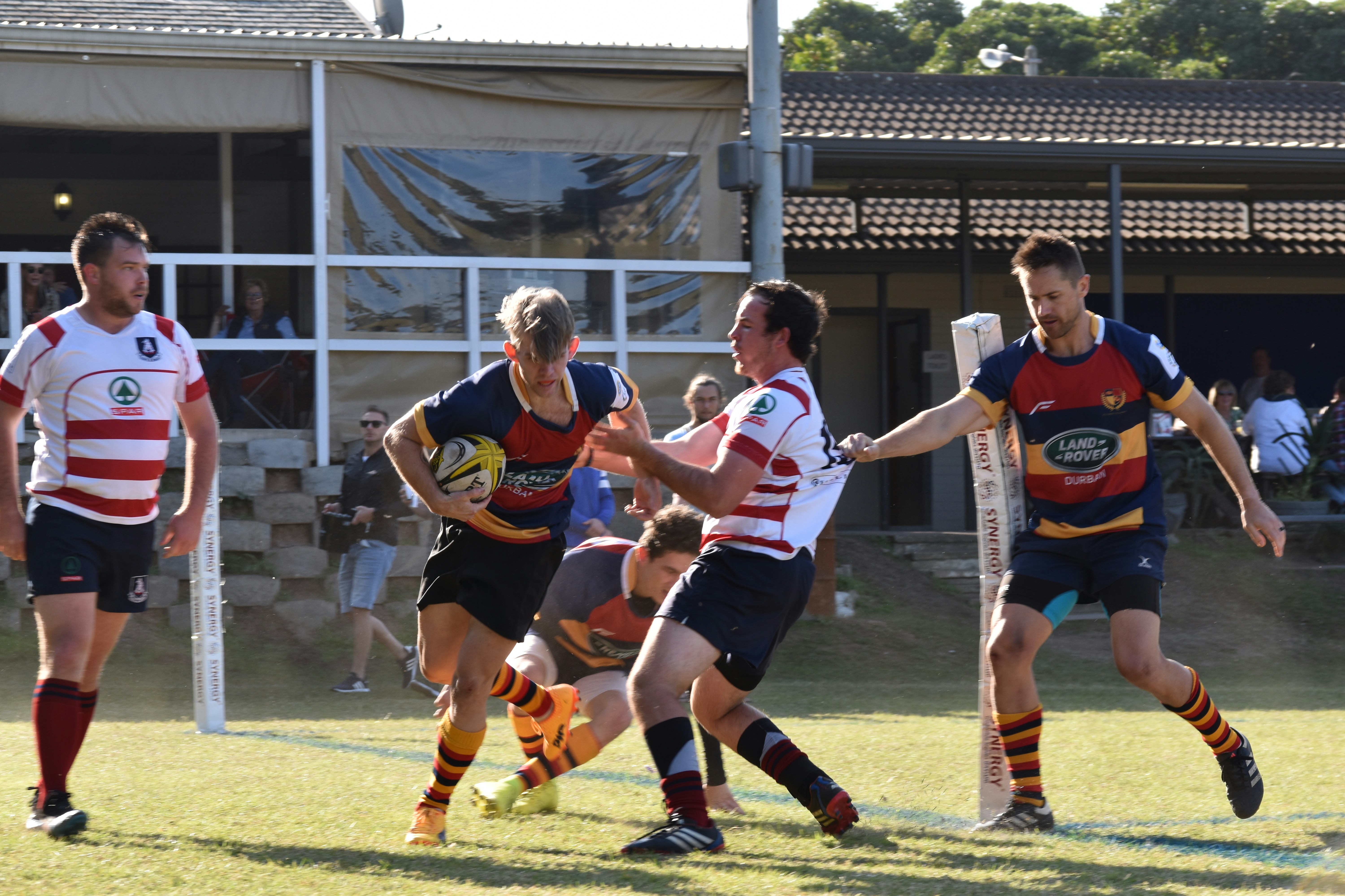 Group of young men playing rugby in South Africa, holding a rugby ball, sunny afternoon, in club colours.