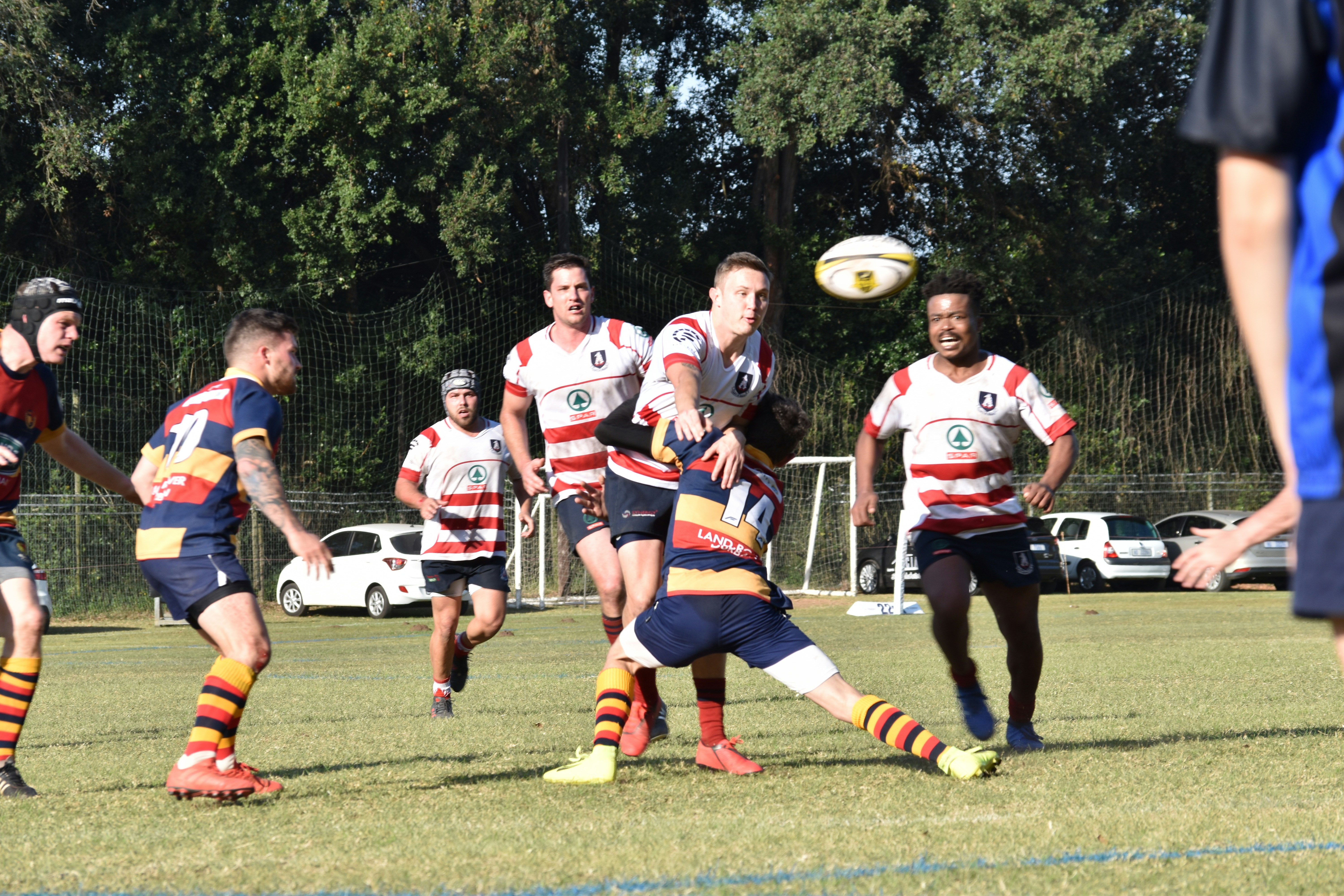 A Hillcrest Villager number 14 pulls a balletic move to stop the Westville Old Boy rugby player going anywhere with the ball, causing the WOB to throw the ball to his team mate directly in front of the camera.