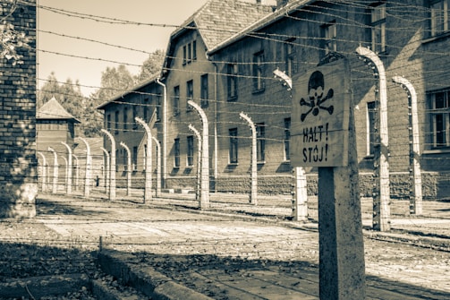 A yard enclosed with barbed wire and brick buildings in the background, featuring a sign with a skull and crossbones warning.
