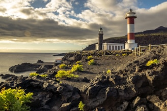 white and red lighthouse on rocky hill near sea under cloudy sky during daytime