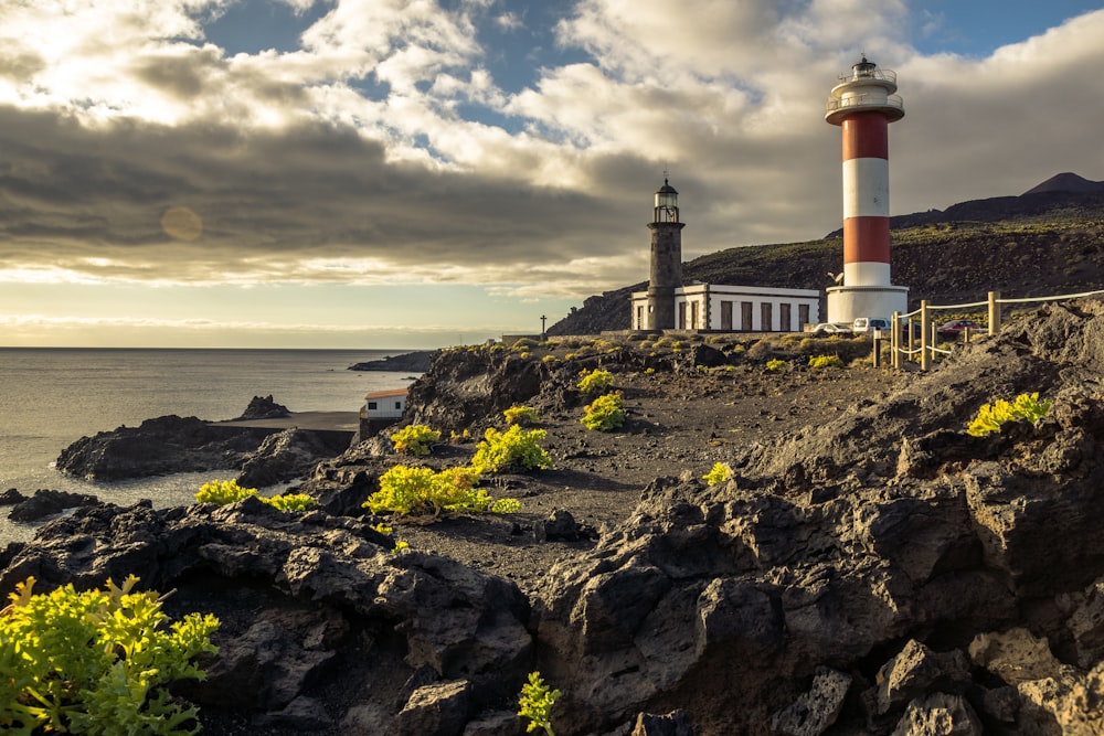 white and red lighthouse on rocky hill near sea under cloudy sky during daytime