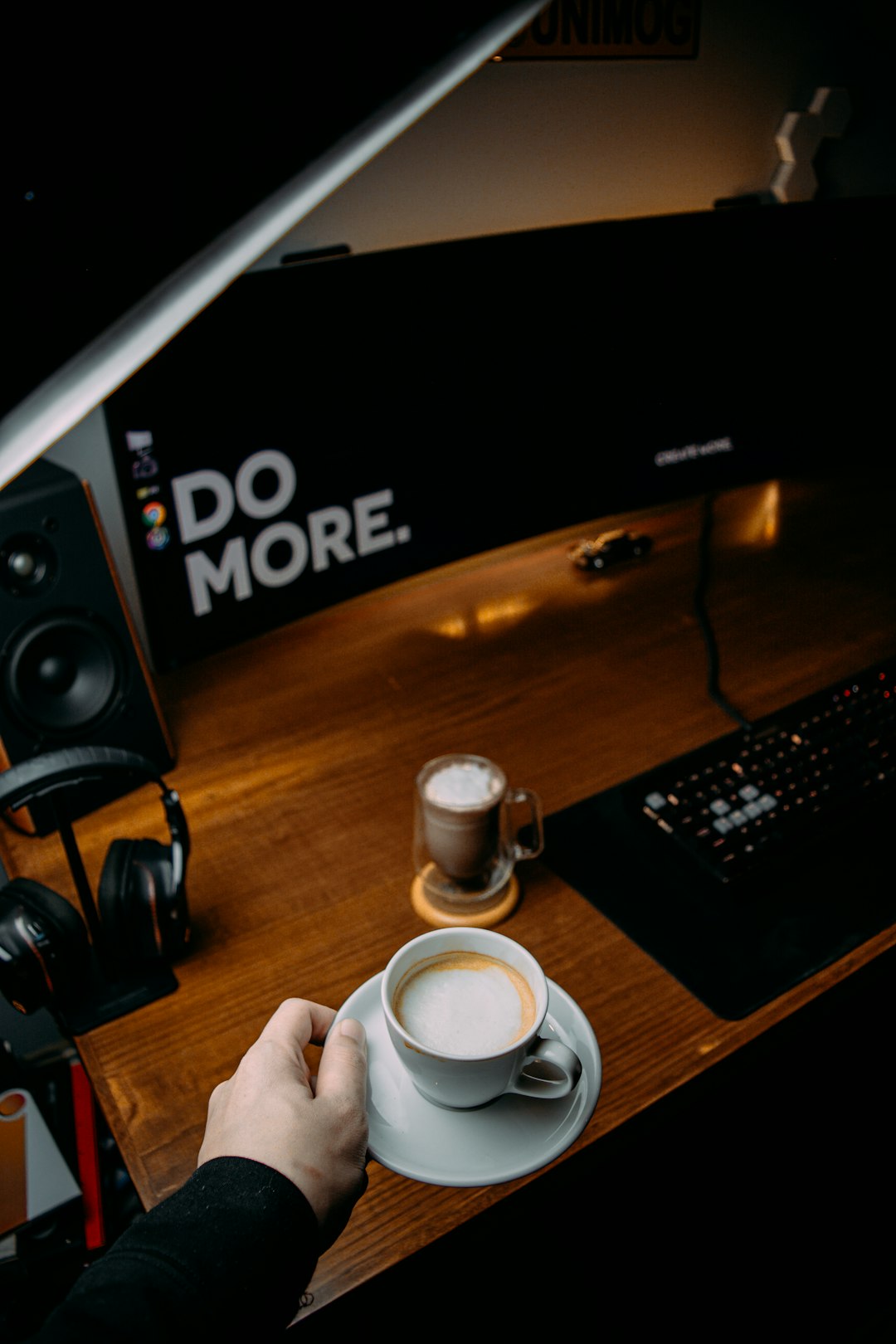 person holding white ceramic mug near black computer keyboard and black flat screen computer monitor