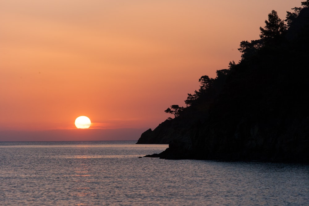 silhouette of mountain near body of water during sunset