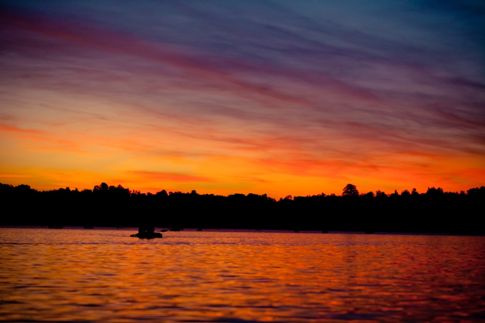 silhouette of 2 people riding boat on sea during sunset