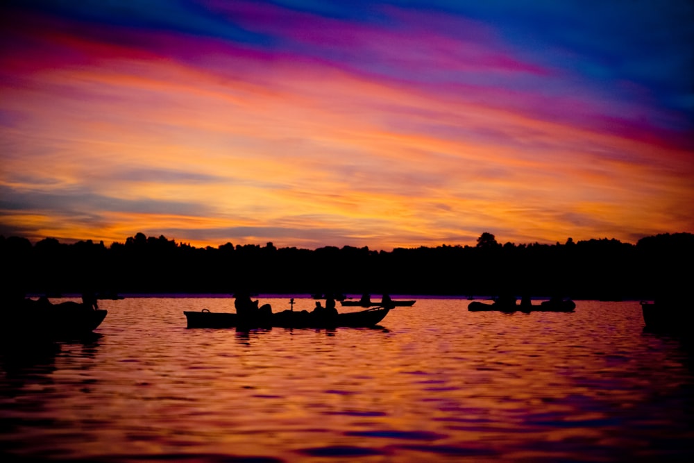 Silueta de la gente que monta el barco en el lago durante la puesta del sol