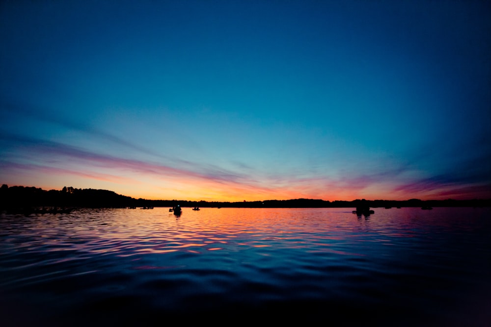 silhouette of people on body of water during sunset