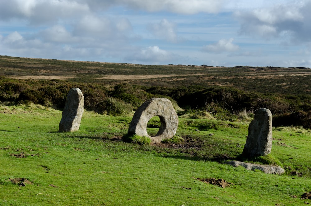 gray rock formation on green grass field under white clouds during daytime