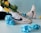 A pair of white high-top sneakers with black swoosh logos are adorned with vibrant blue and yellow flowers. The shoes are set against a light blue background, suggesting a playful and artistic composition.