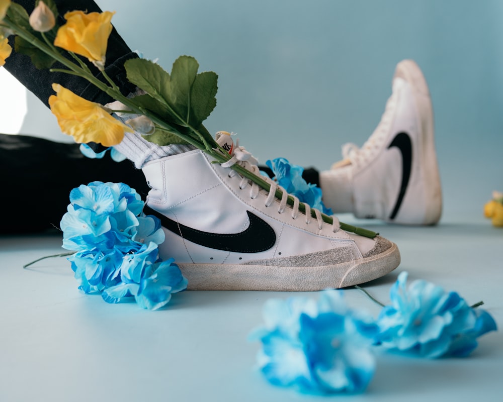 Weiße und schwarze Nike Sneakers neben blauen Blumen