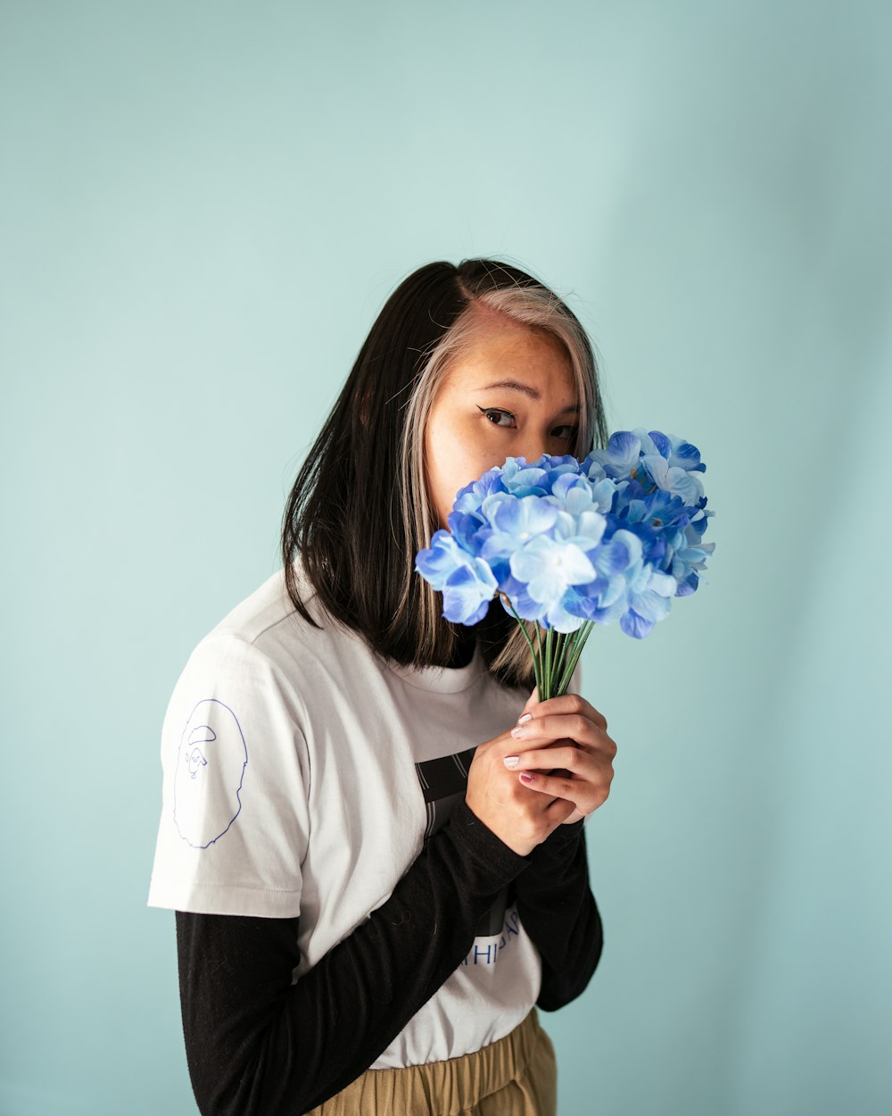 woman in white long sleeve shirt holding blue flower