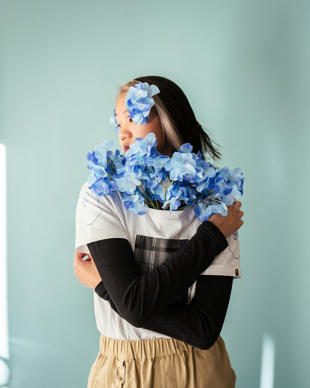 woman in white long sleeve shirt holding blue flowers