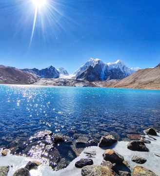 rocky shore with mountain in distance under blue sky during daytime