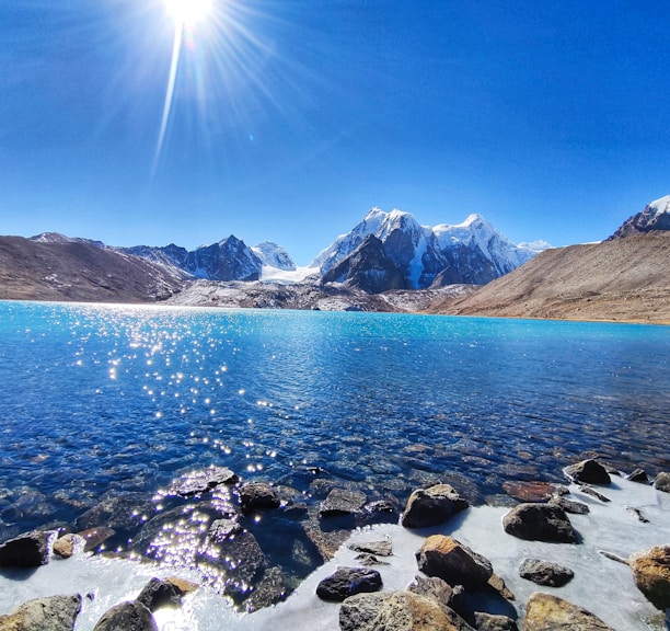 rocky shore with mountain in distance under blue sky during daytime