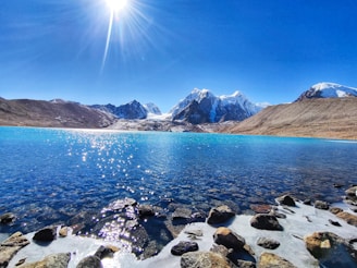 rocky shore with mountain in distance under blue sky during daytime