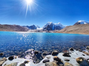 rocky shore with mountain in distance under blue sky during daytime