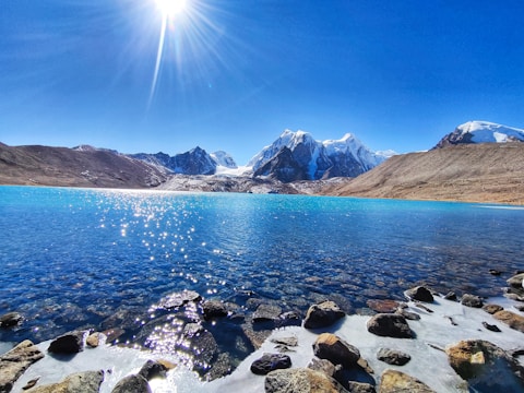 rocky shore with mountain in distance under blue sky during daytime