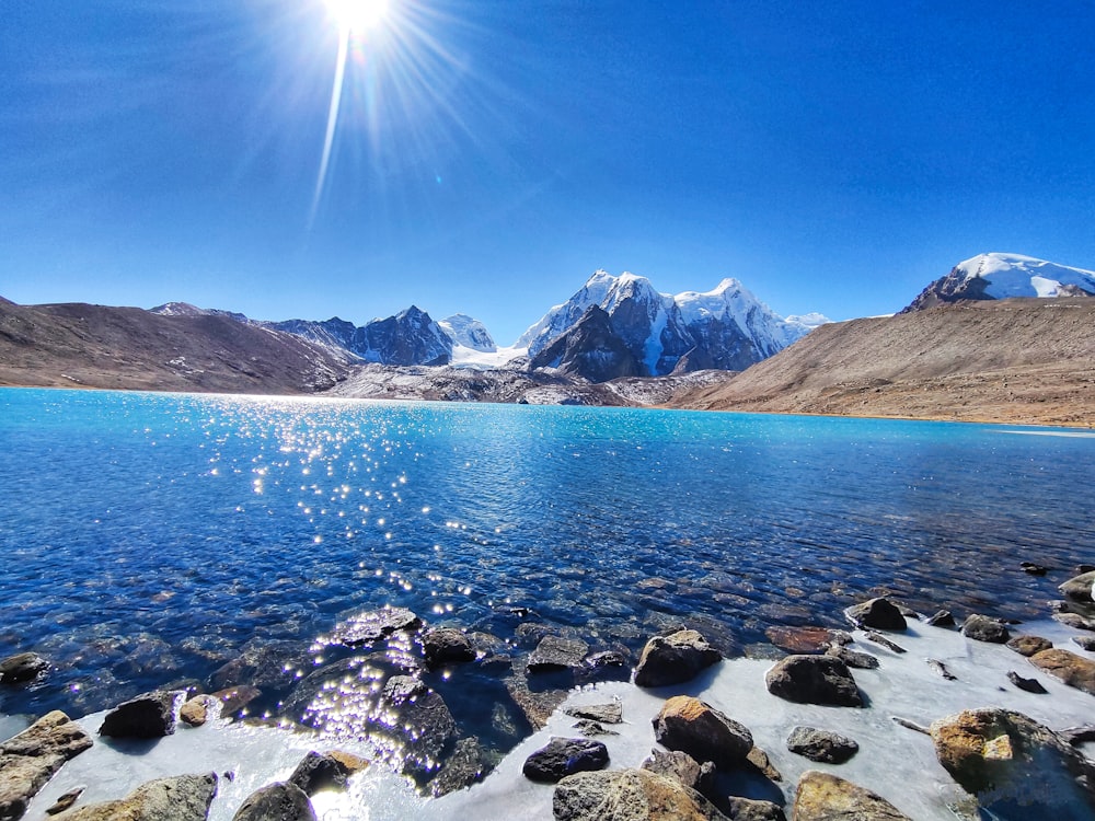 rocky shore with mountain in distance under blue sky during daytime