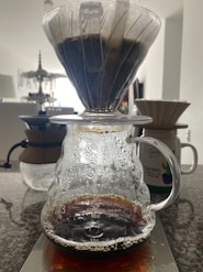 Close-up of a V60 coffee dripper with fresh coffee dripping into a glass carafe.
