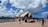 The image captures a view of the Sydney Opera House on a partially cloudy day. The iconic architecture with white, sail-like structures is prominently displayed against a vibrant blue sky filled with fluffy clouds. In the foreground, people are walking and enjoying the area, with a waterfront and cityscape visible in the background.