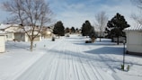 A snow-covered residential driveway with tire tracks left behind.