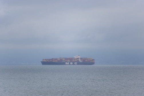 Cargo ship loaded with containers sailing across a calm ocean at sunset.