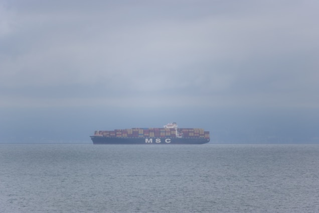 A cargo ship loaded with containers navigating through calm waters.