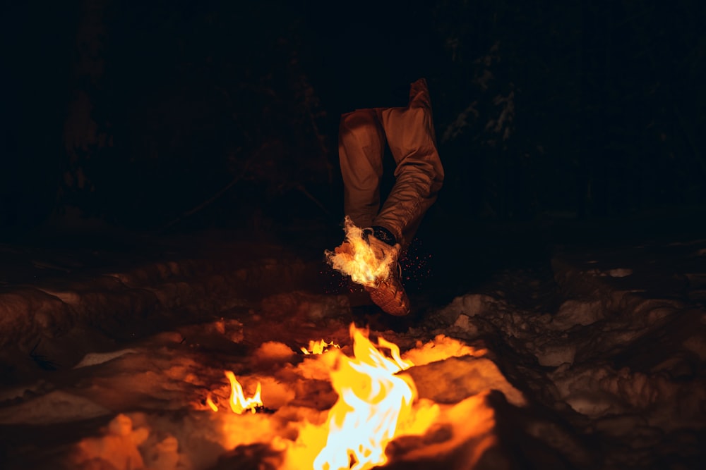man in brown jacket sitting on ground with fire