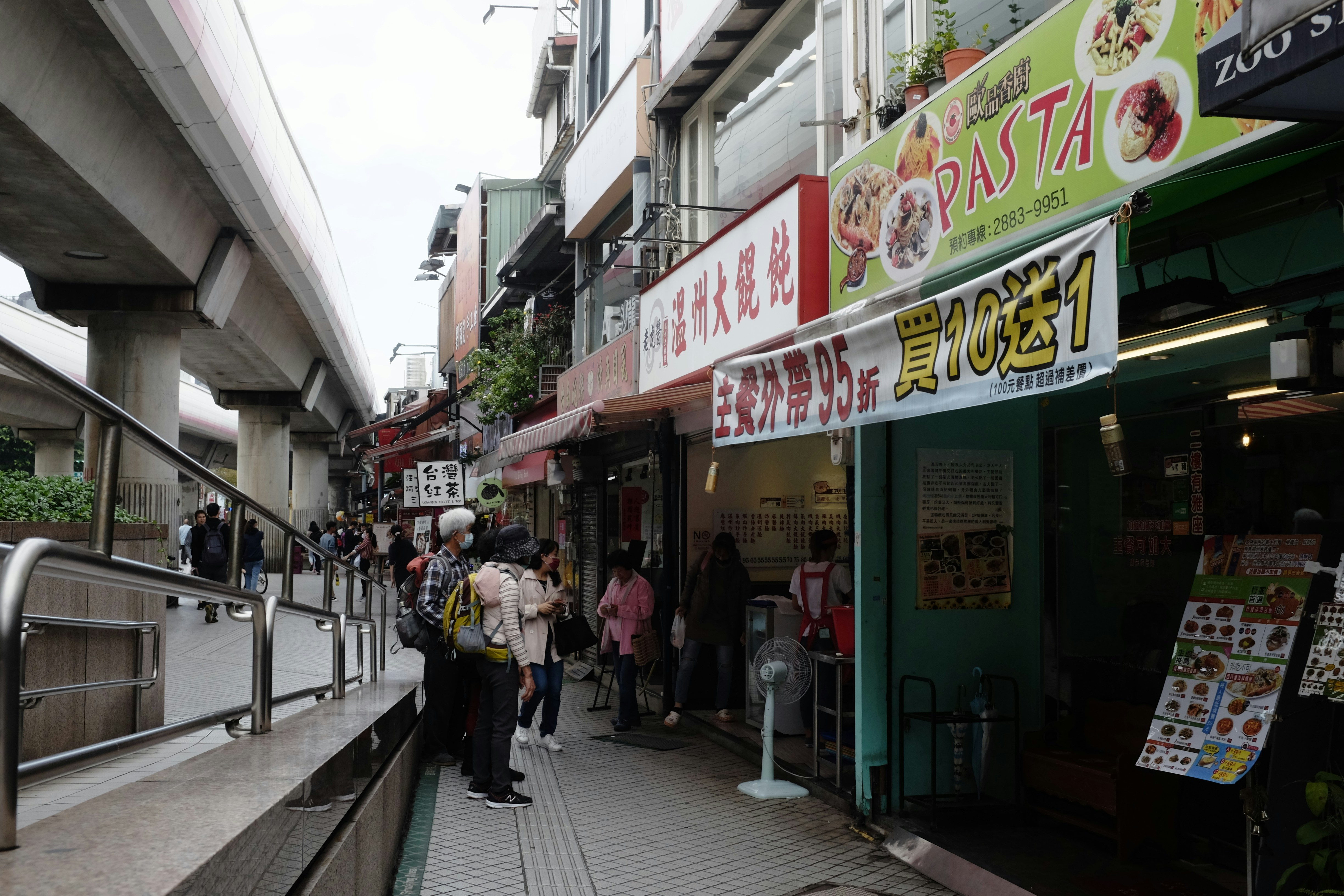A busy street-level view of a CBD showing retail shops with offices above and pedestrians on the sidewalk - Central business district