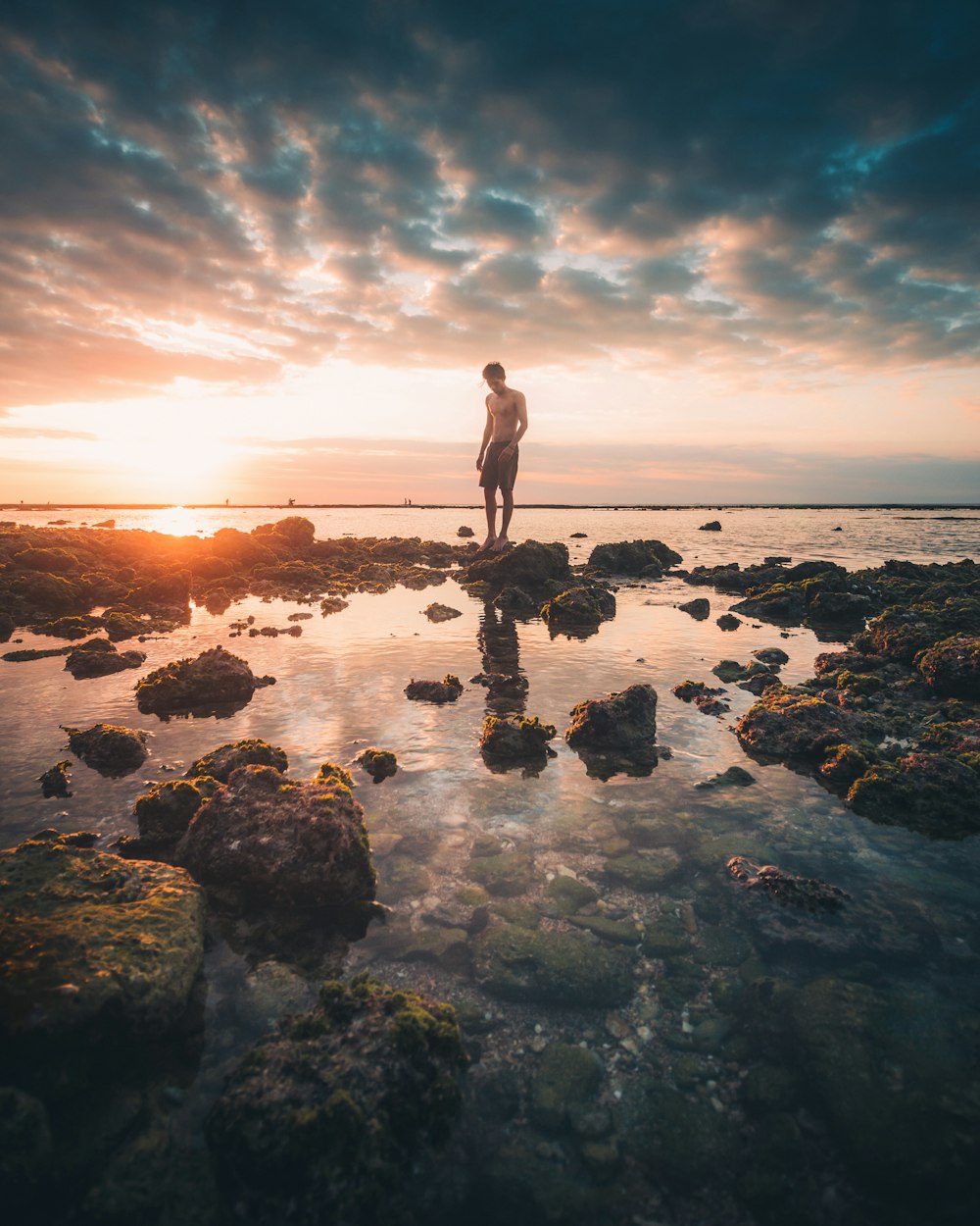 man standing on rocky shore during sunset