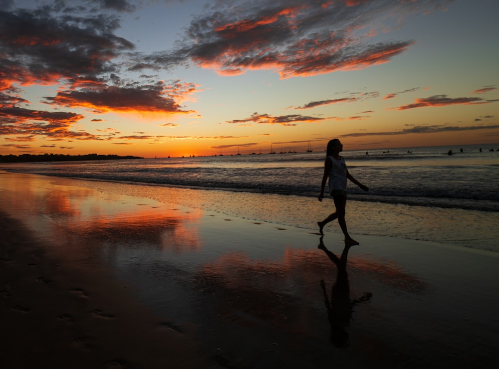 femme en robe noire marchant sur la plage pendant le coucher du soleil