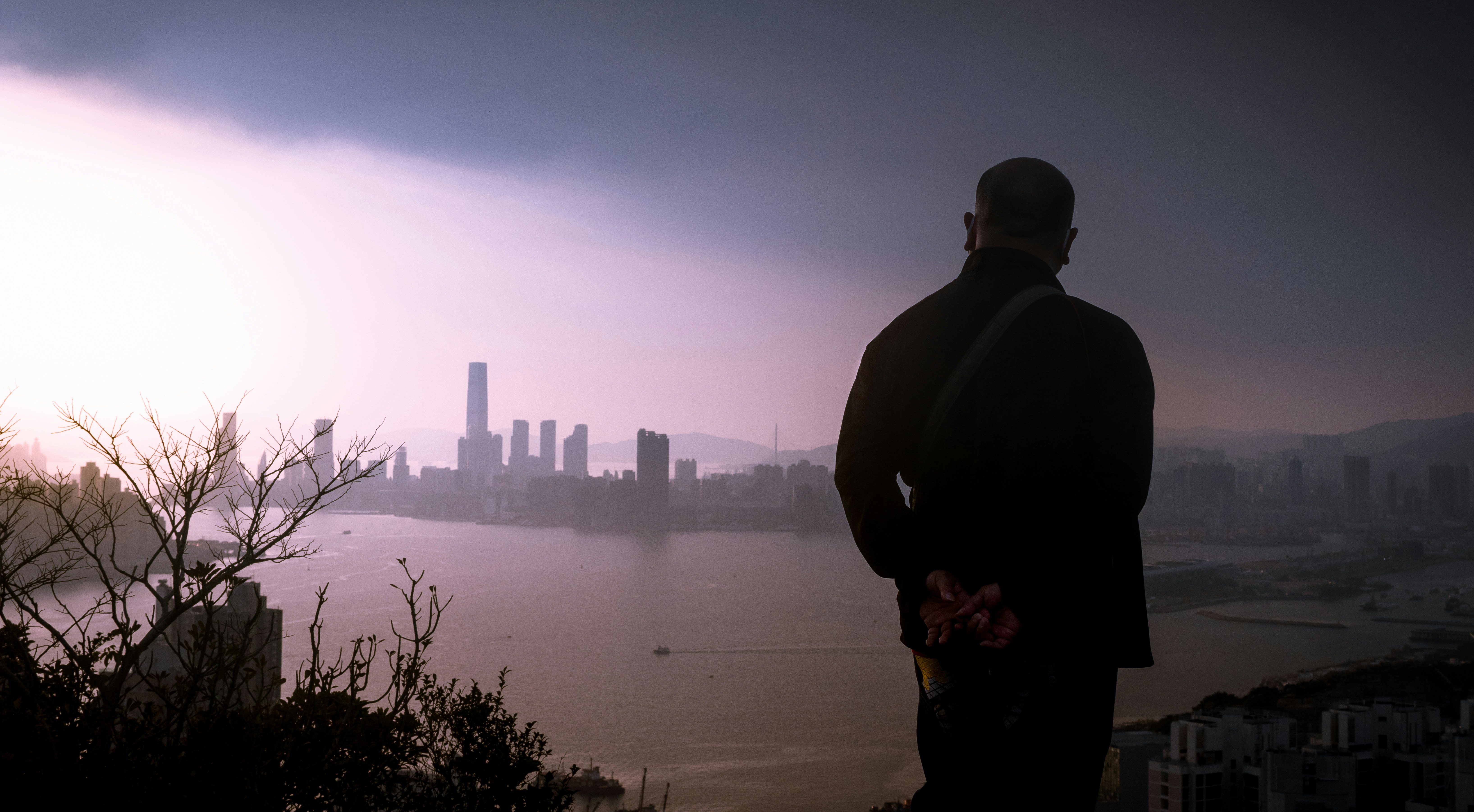 man in black jacket standing on the edge of a building looking at the city during, The thinker