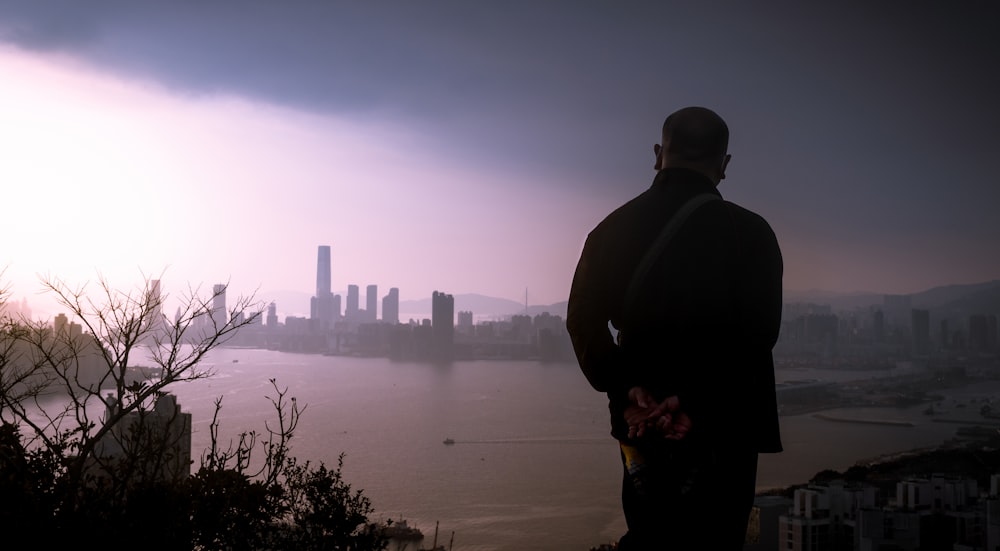 man in black jacket standing on the edge of a building looking at the city during