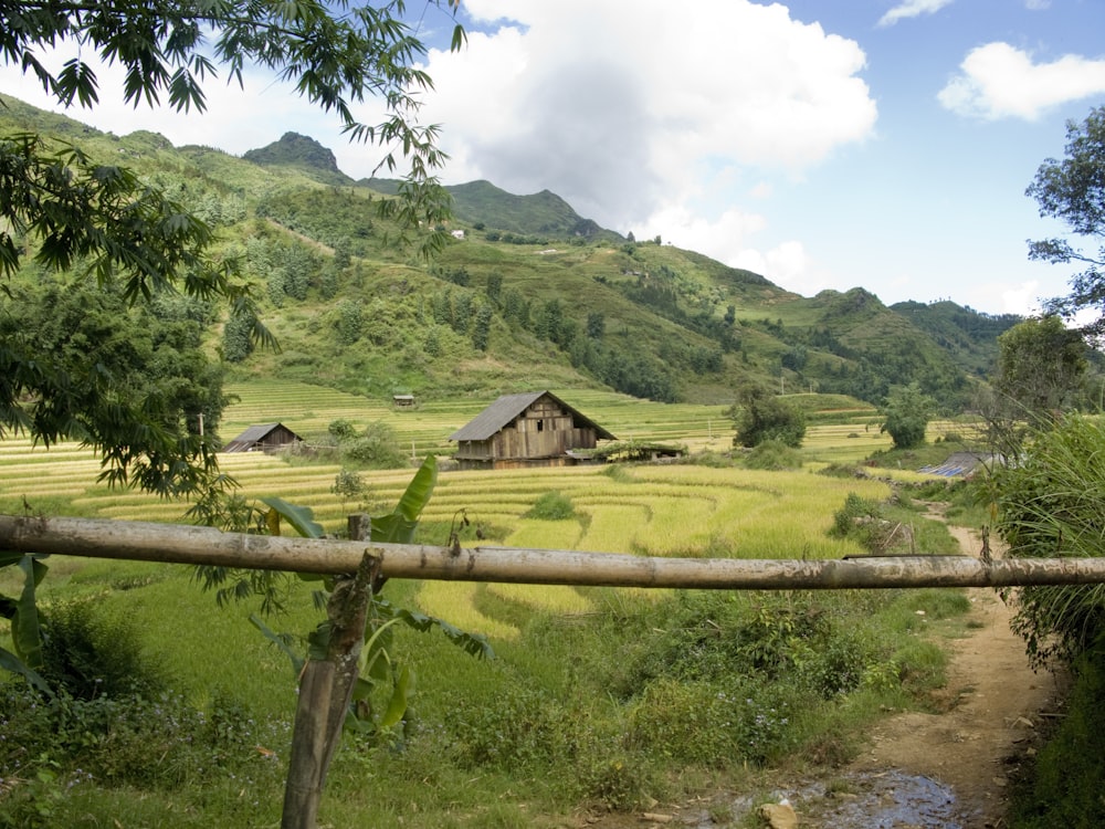 brown wooden house on green grass field near green mountains under white clouds during daytime