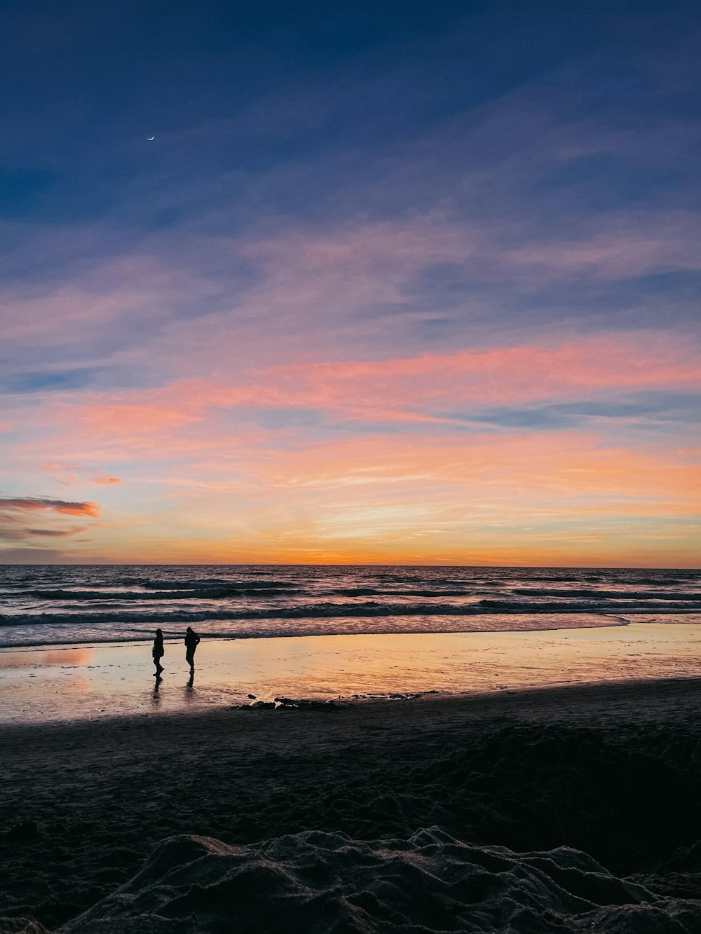 silhueta de 2 pessoas caminhando na praia durante o pôr do sol