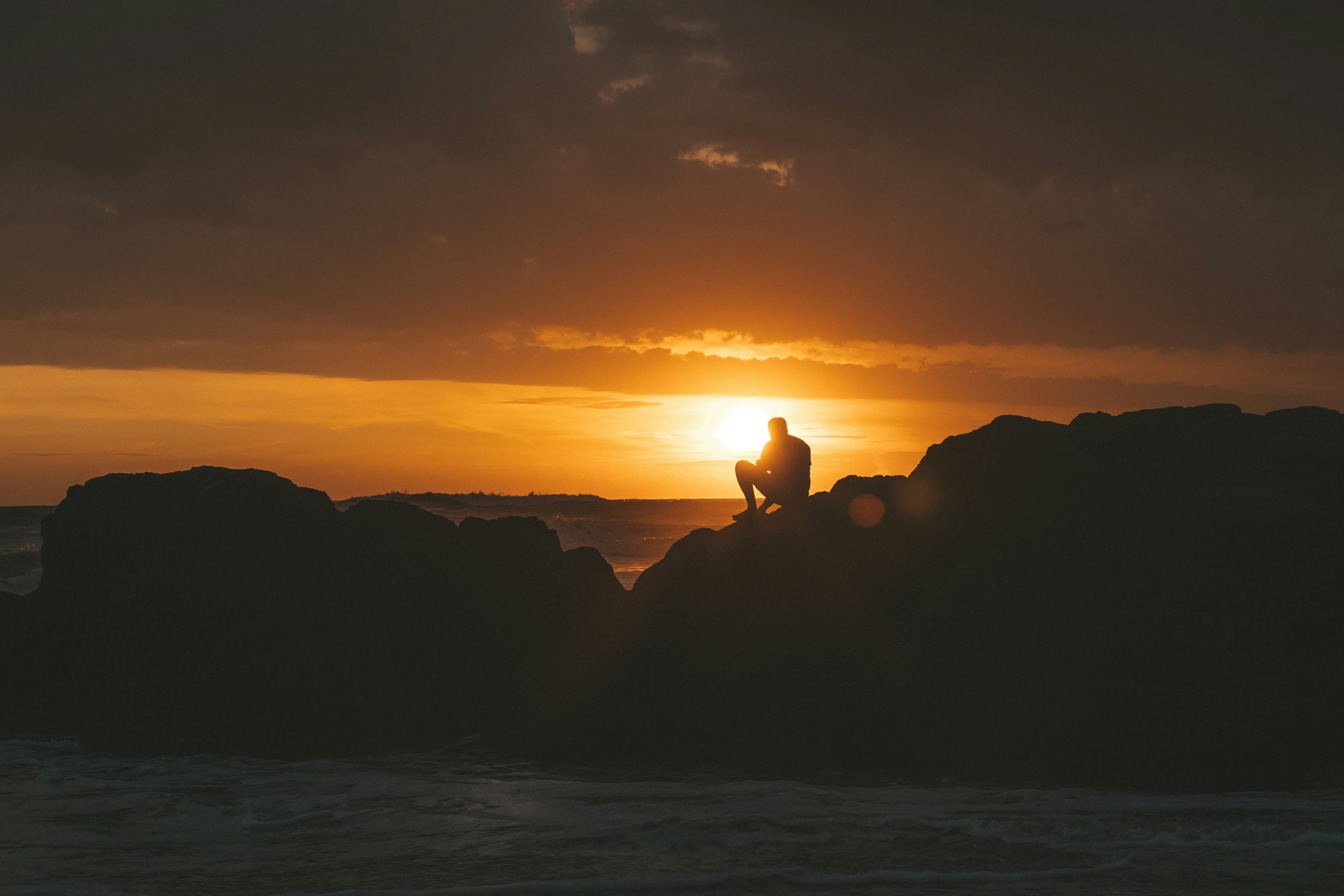 silhouette of rock formation on sea during sunset