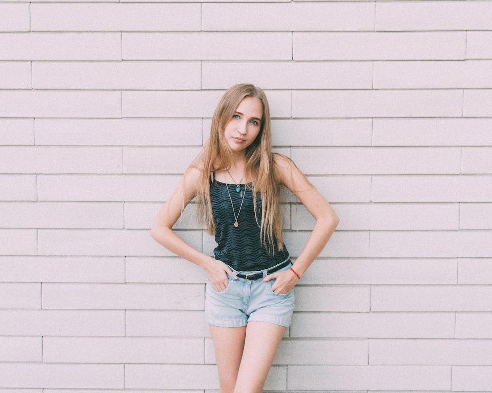 woman in blue denim shorts standing beside white wall