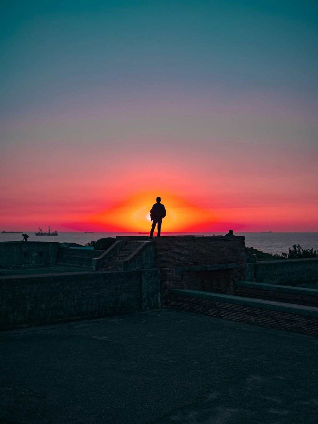 silhouette of person standing on concrete fence during sunset