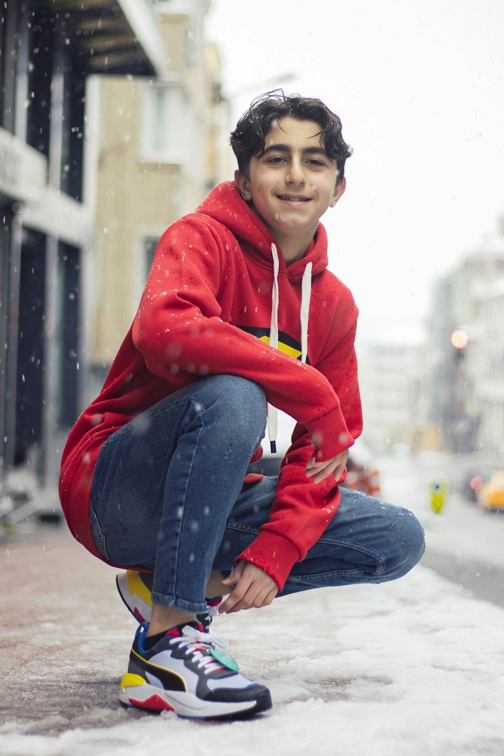 Hombre con sudadera con capucha roja y jeans vaqueros azules sentado en el piso de concreto