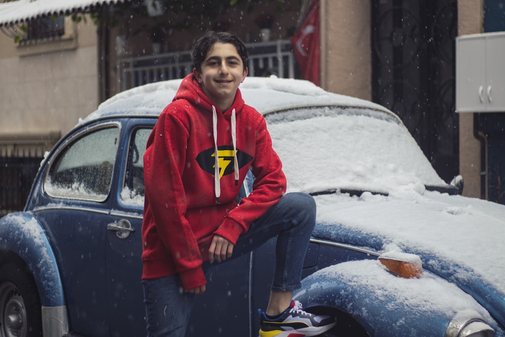 man in red and white zip up jacket sitting on blue car