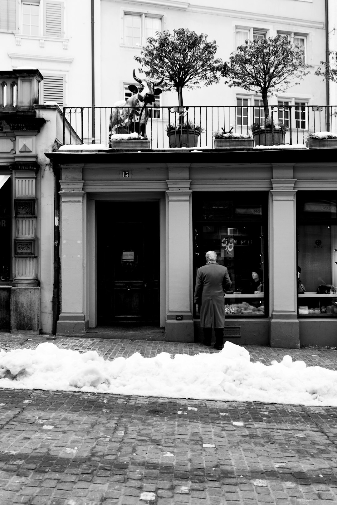 grayscale photo of man in black coat standing near building during daytime